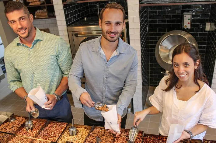 Greg and Evan scooping roasted nuts with the owner of Graem Roasters.
