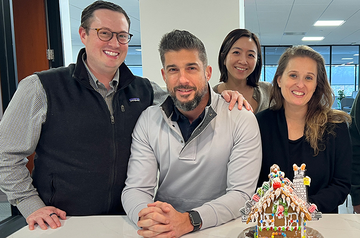 Few employees standing around a gingerbread house on a counter