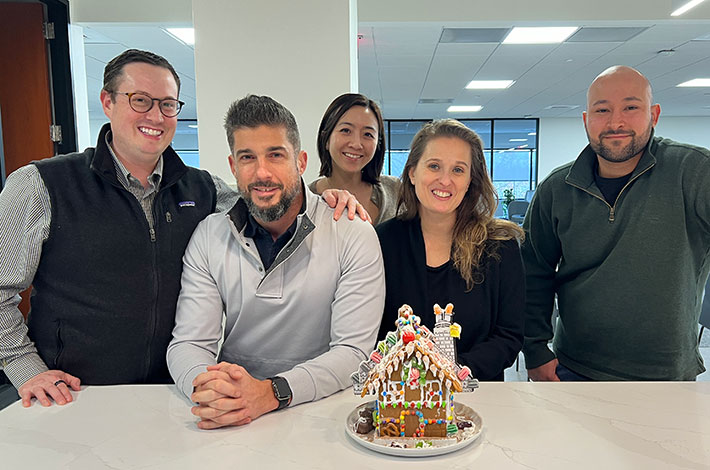 Few employees standing around a gingerbread house on a counter
